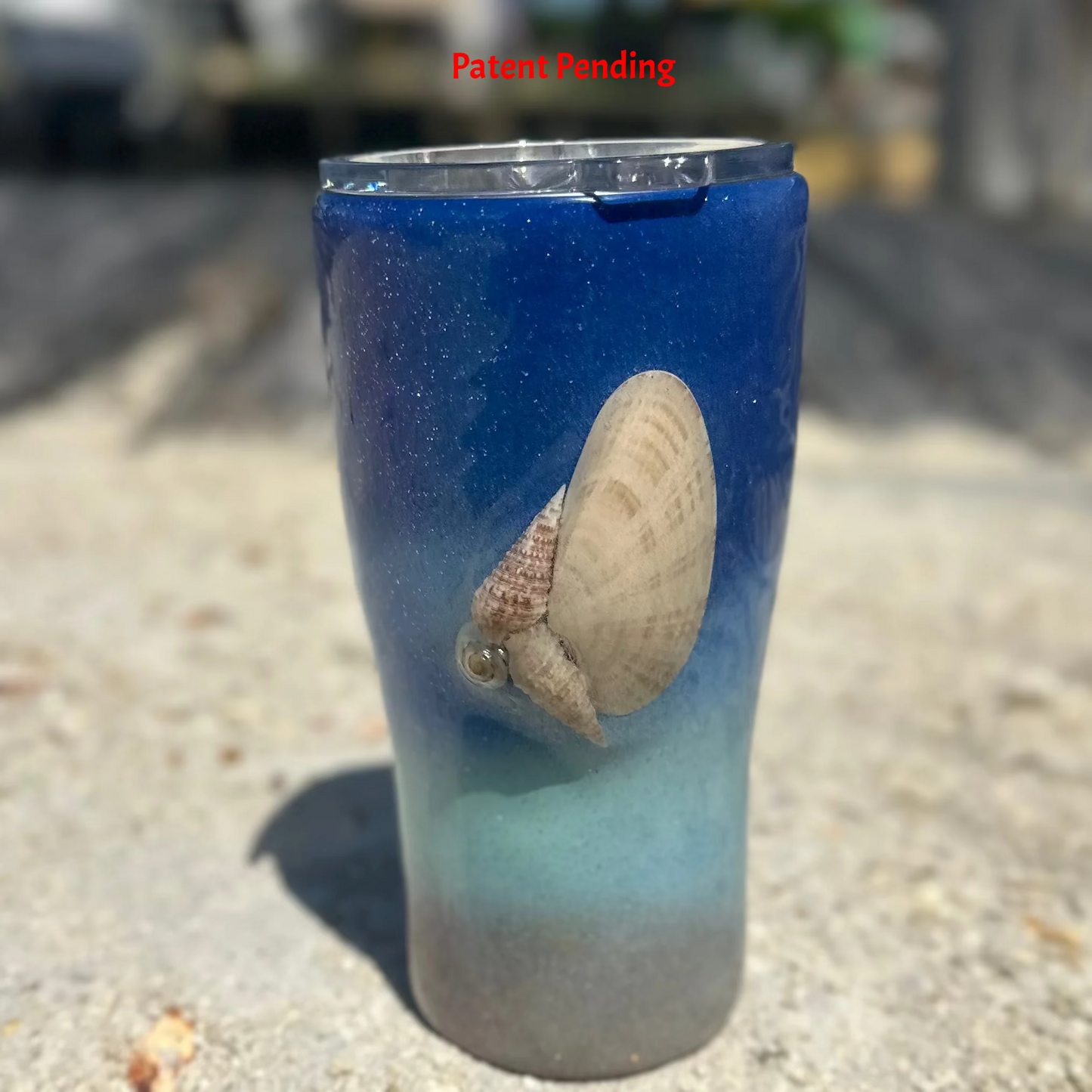 Blue ombre Saltwater Sips™ 20oz seashell tumbler front view, dock and water in background, real Florida seashell, Patent Pending, handcrafted in South Florida