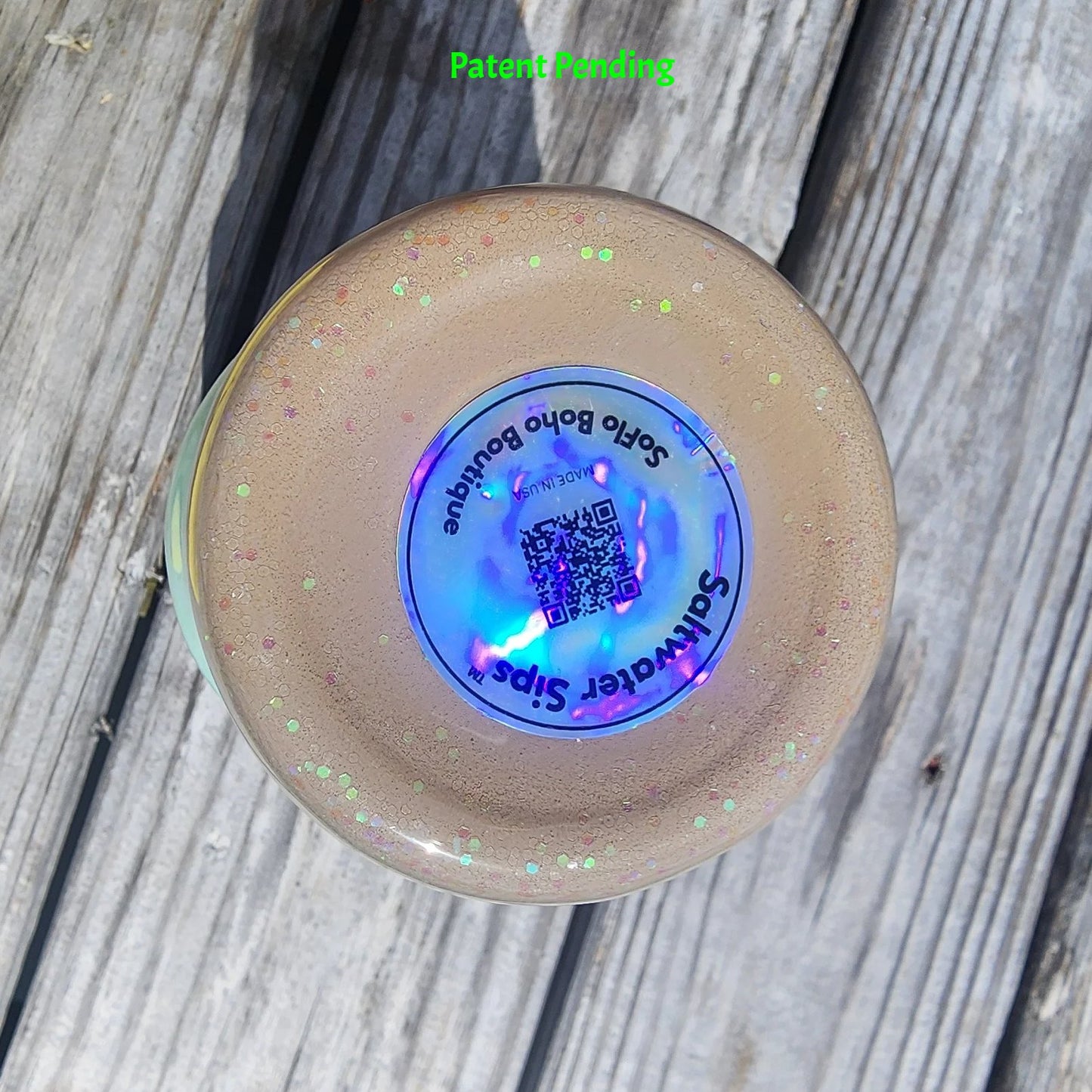 Bottom view of Caribbean Glow Shell Glitter 30oz tumbler on South Florida marina dock showing holographic Saltwater Sips™ brand label with QR code and SoFlo Boho Boutique branding. Made in USA, Patent Pending.