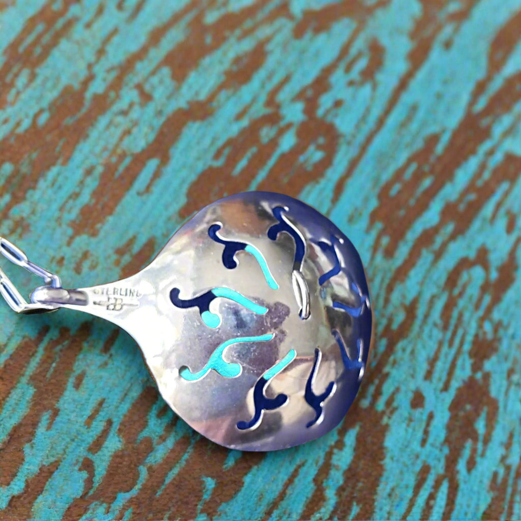 Silver spoon pendant with blue accents on a textured blue and brown background