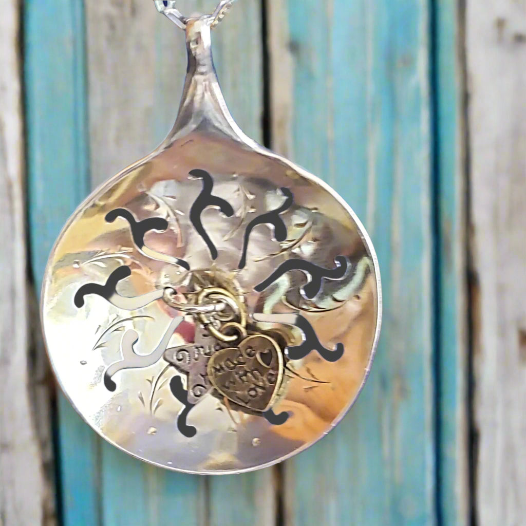 Silver spoon pendant with heart charm against a wooden background