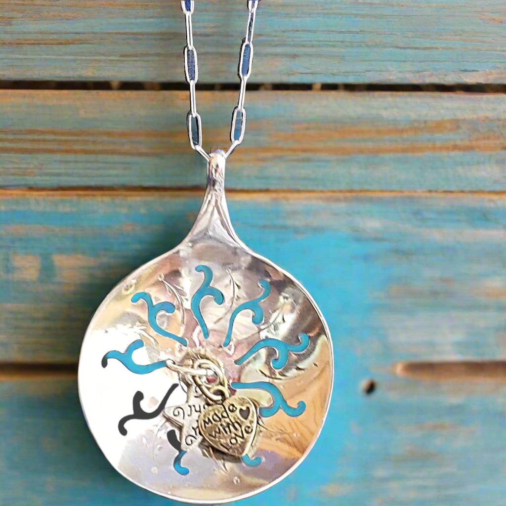 Silver spoon pendant with blue and black designs on a wooden background