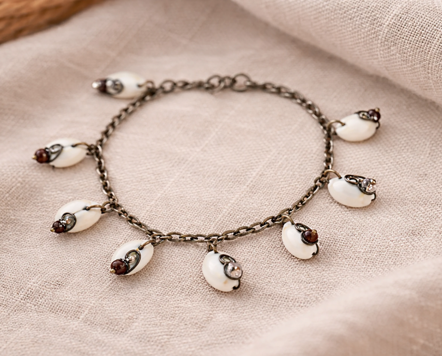 Handmade cowrie shell bracelet on neutral linen surface with vintage chain and glass bead details