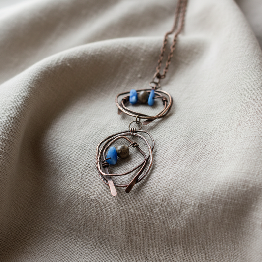 Close-up of handmade copper wire-wrapped pendant necklace with brown jasper and blue abalorios beads, resting on linen fabric