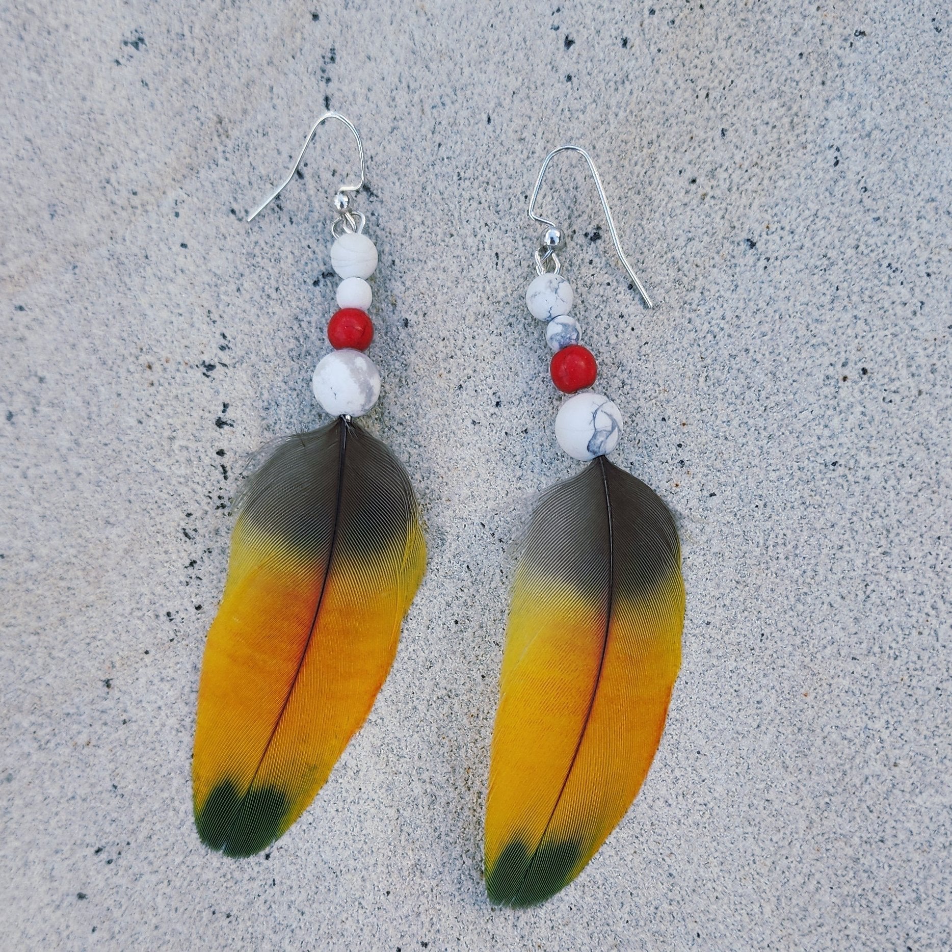 Yellow Feather Earring with white howlite and coral red bead laying flat