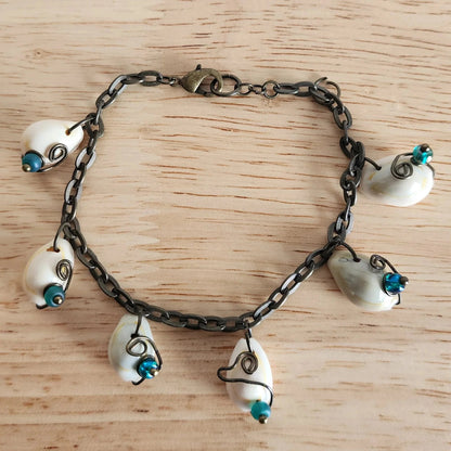 Shell charm bracelet laid flat on wood surface with alternating green and blue beads and oval link chain