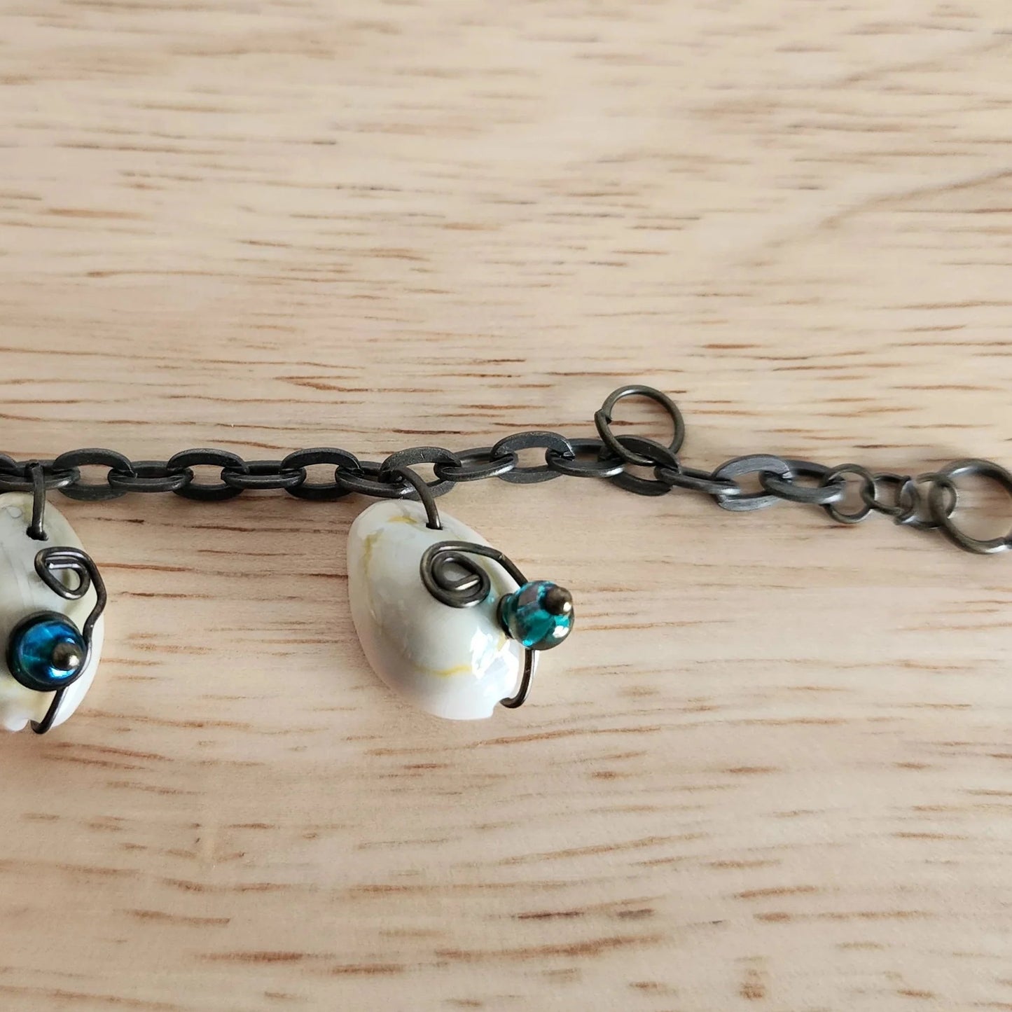 Close up detail of wire wrapped shell charm bracelet with green and blue glass beads on oxidized chain