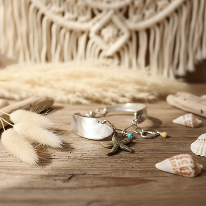 Silver bracelet with charms on a wooden surface with dried plants and shells.