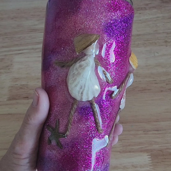 Video: hand holding a pink and purple glitter shell people tumbler with a real seashell figure