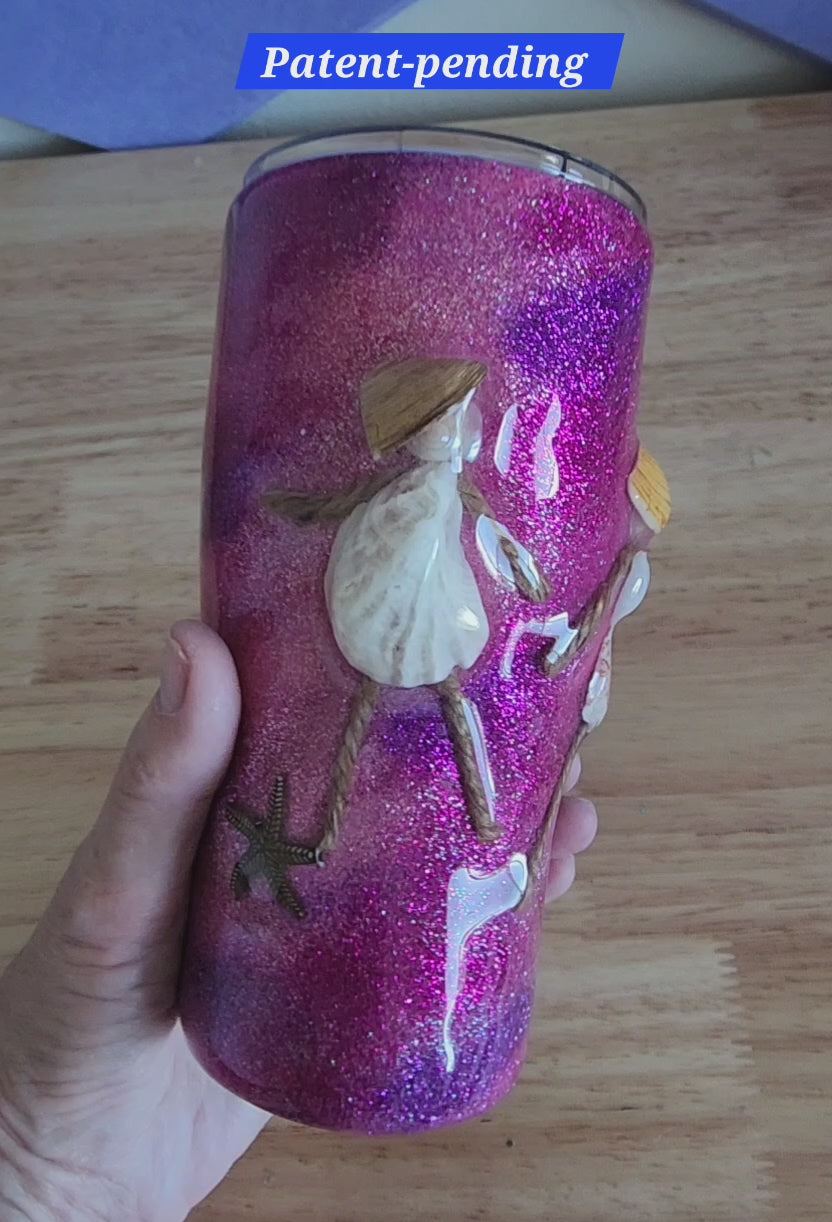 Video: hand holding a pink and purple glitter shell people tumbler with a real seashell figure