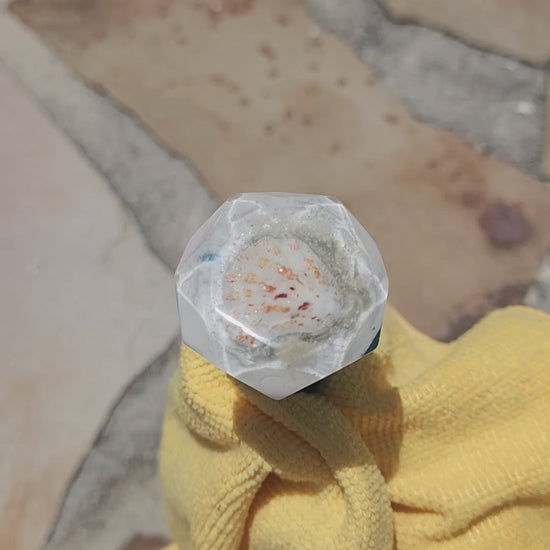 Birds-eye view of the multi-faceted crystal top of a handmade resin bottle stopper, highlighting the embedded shimmering details and crisp white crest