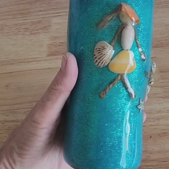 Video: hand holding a teal 20oz shell people tumbler with real seashell details