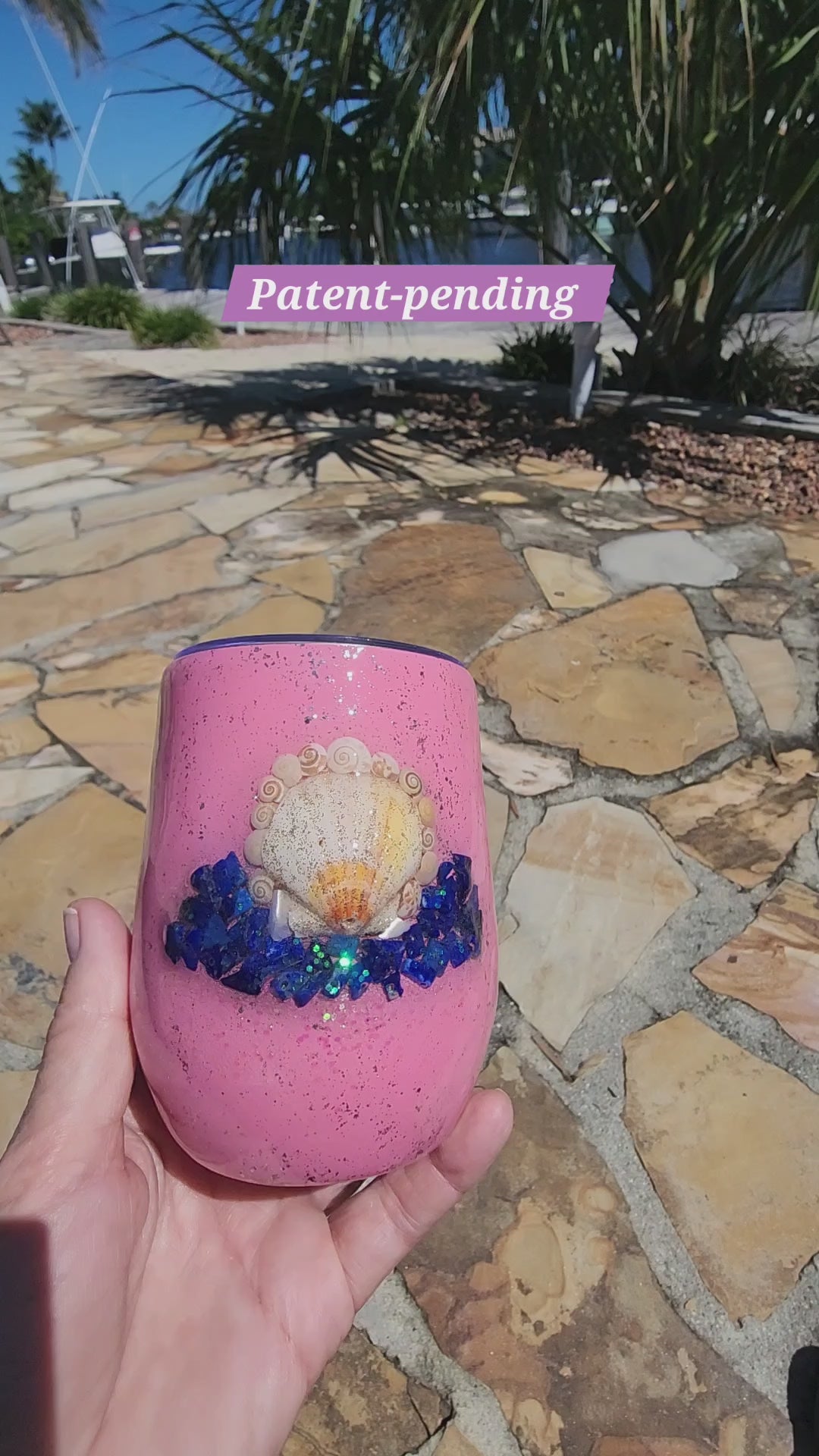 Video of a handmade pink 12oz seashell wine tumbler with lapis lazuli chips held in hand outdoors by the water