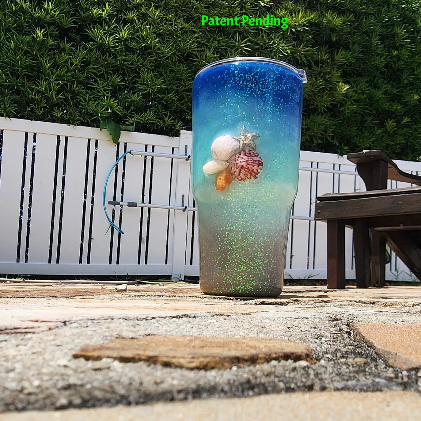 Caribbean Glow Shell Glitter 30oz tumbler front view with real fighting conch, red, spiral and olive seashells, silver starfish charm and holographic iridescent glitter shifting green, teal, turquoise and blue. Saltwater Sips™ by SoFlo Boho Boutique, Patent Pending, handcrafted in South Florida.
