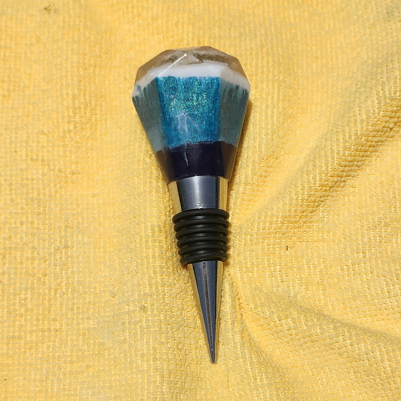 Handmade multi-faceted turquoise and dark blue resin wine bottle stopper with a white top layer, set on a tapered alloy metal base with black rubber gaskets.