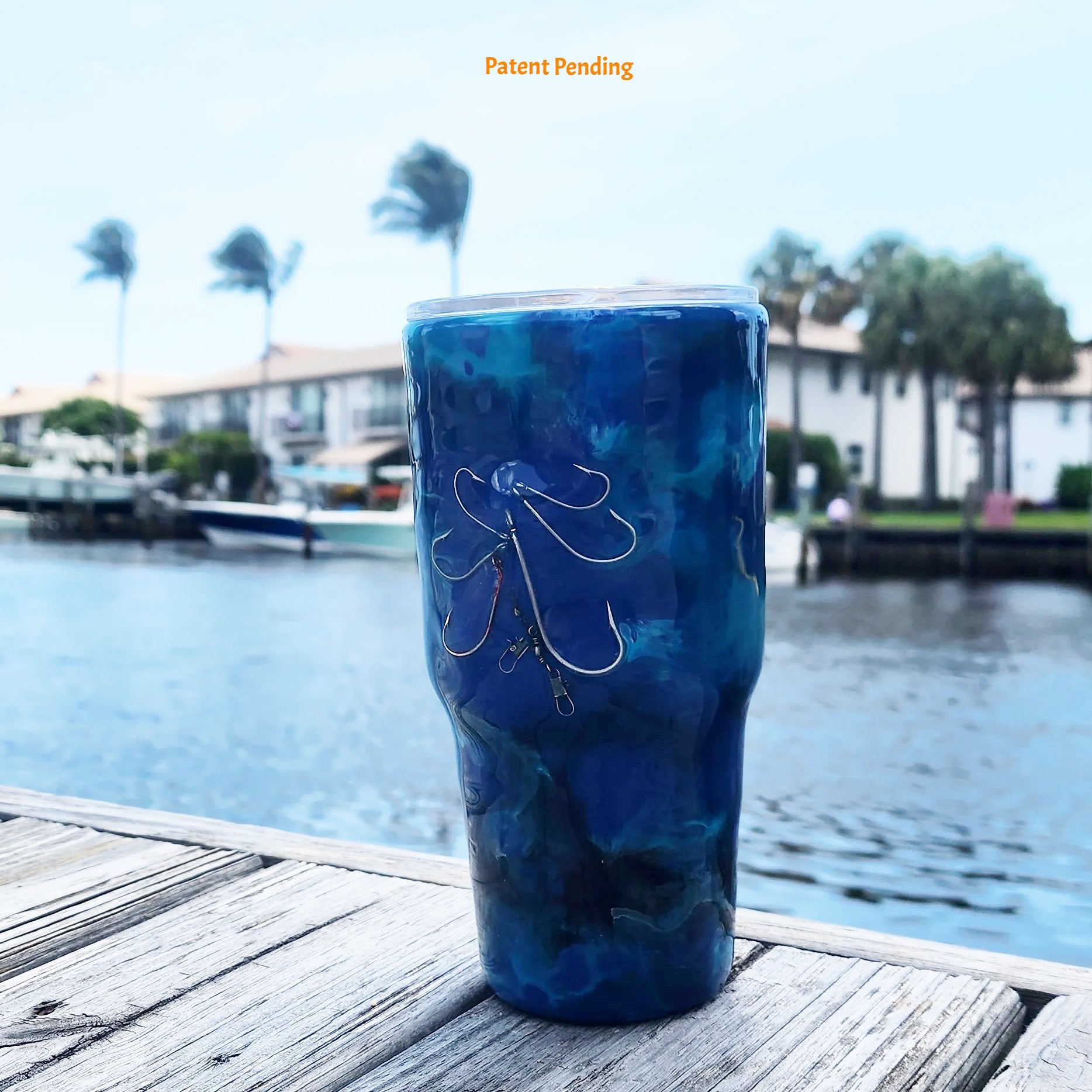 Blue Open Water front view fishing hook tumbler photographed at waterfront dock, showing deep cobalt and teal handmade 30oz coastal drinkware