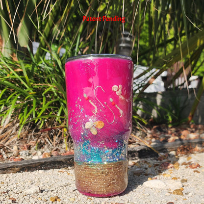 Magenta Tide 30oz Hook & Tumble fishing tumbler for women on sandy beach showing real seashells and fish hooks embedded in hot pink epoxy resin with rope wrapped base