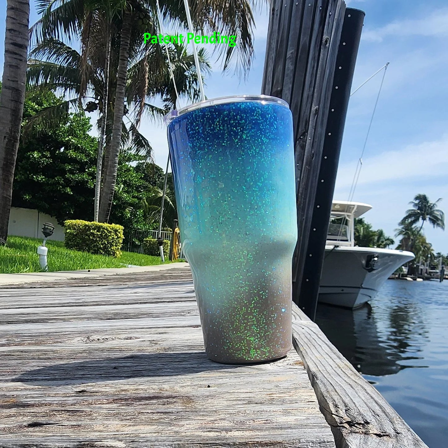 Back view of Caribbean Glow Shell Glitter 30oz tumbler on South Florida marina dock showing full deep cobalt blue to crystal turquoise to sandy shore design with holographic iridescent glitter and waterway in background. Saltwater Sips™ by SoFlo Boho Boutique, handcrafted in South Florida, Patent Pending.