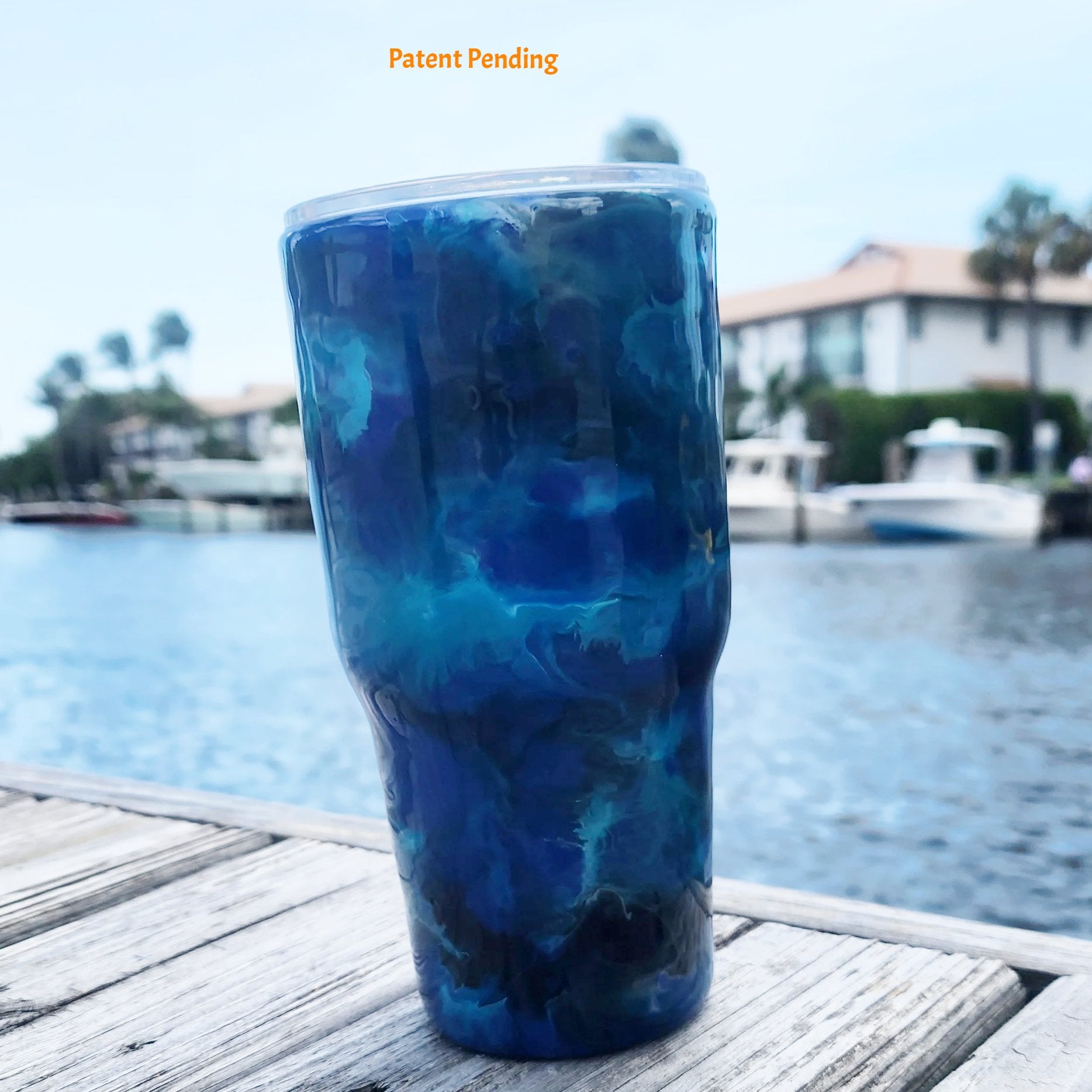Blue Open Water back view fishing hook tumbler photographed at waterfront dock, showing deep cobalt and teal handmade 30oz coastal drinkware