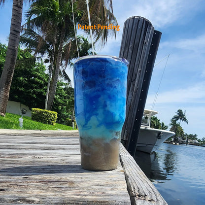 Back view of Crystal Shore Deep 30oz fishing tumbler on South Florida marina dock showing full sandy shore to crystal turquoise to deep cobalt blue ocean design with palm trees and boat in background. Hook & Tumble™ by SoFlo Boho Boutique, handcrafted in South Florida, Patent Pending.