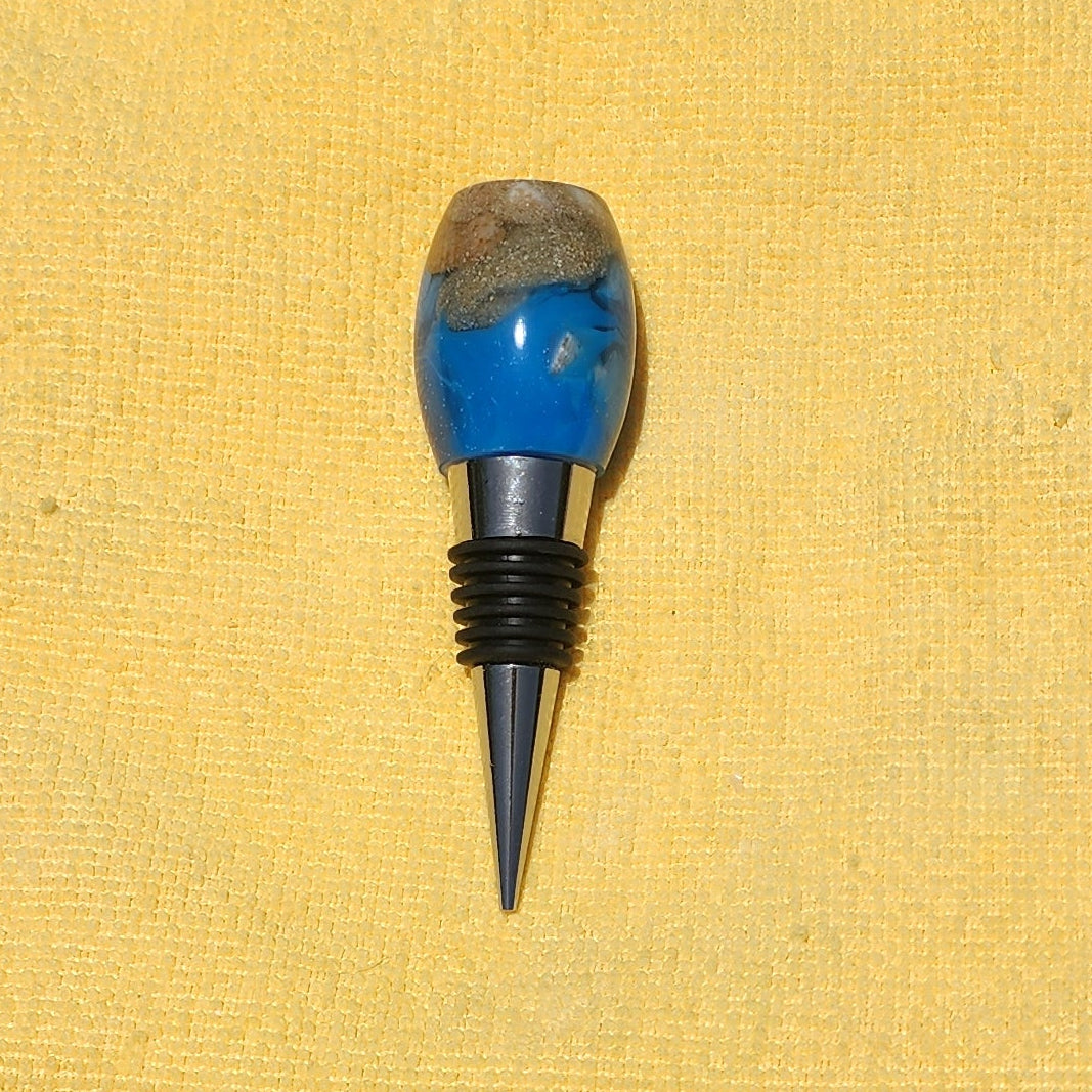 Handmade smooth oval resin wine bottle stopper featuring a realistic blue ocean wave swirl and sandy beach top layer on a polished metal alloy base.