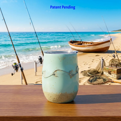 Handmade 12oz steal fishing hook tumbler with real fishing hook and sand on a table by the ocean with a wooden fishing boat