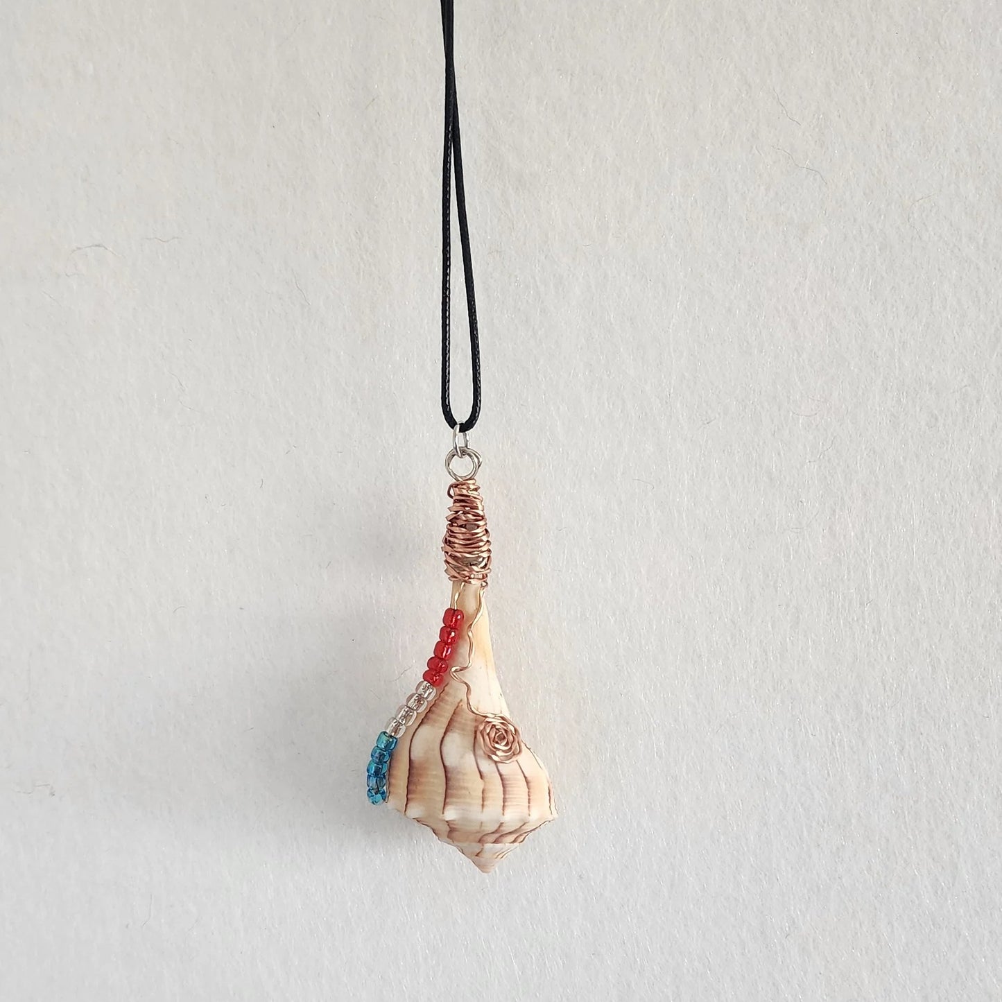 Lightning Whelk seashell pendant necklace hanging on black cord, full view showing copper wire wrap and shell point