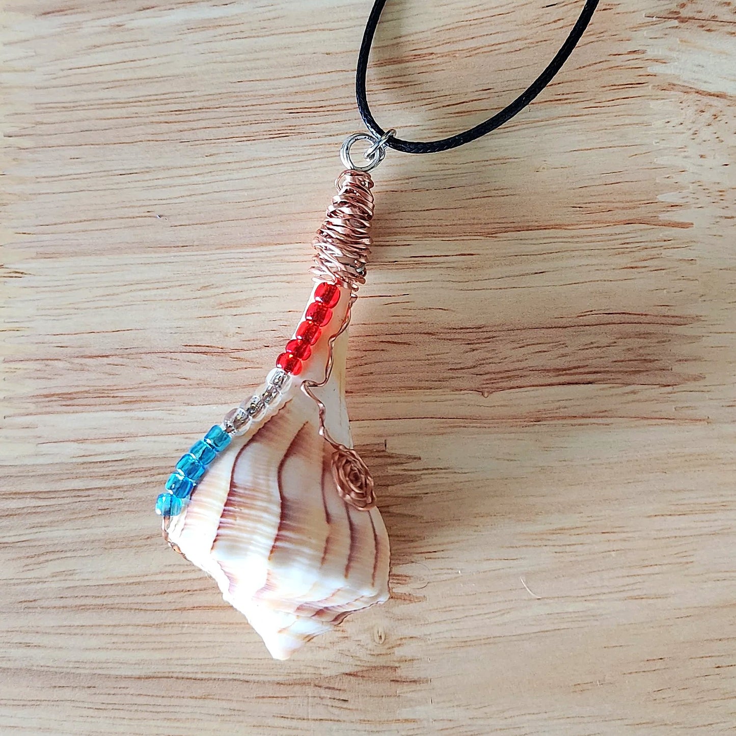 Close up of wire wrapped seashell pendant showing copper coil bail and glass bead detail on black cord