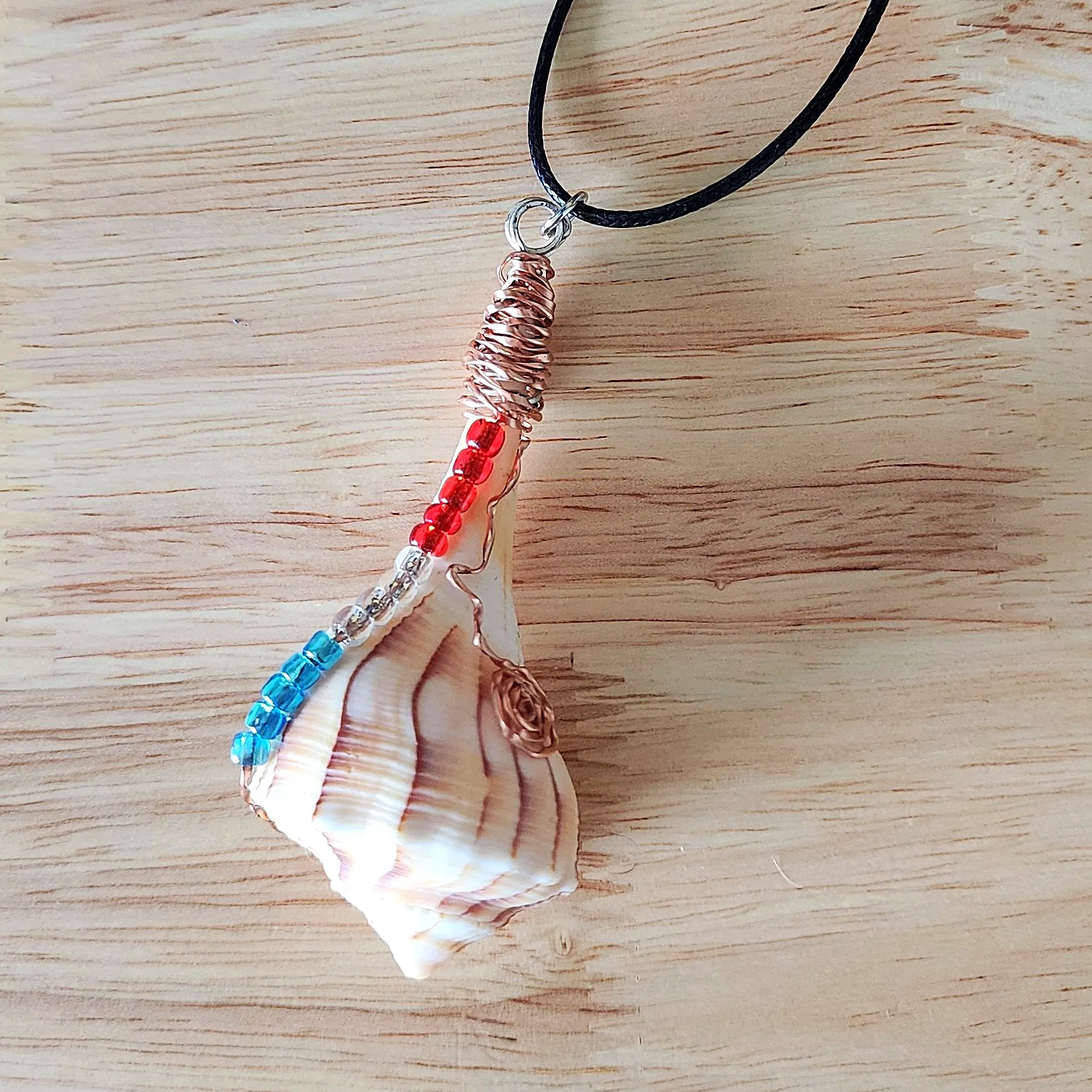 Close up of wire wrapped seashell pendant showing copper coil bail and glass bead detail on black cord
