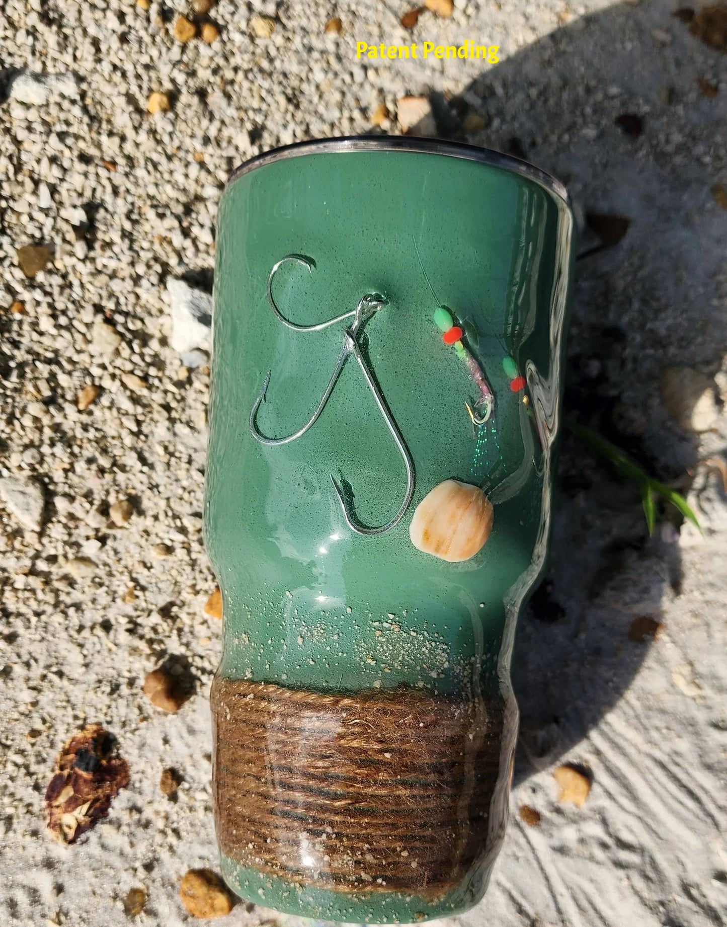 Marsh Tide 30oz Hook & Tumble fishing tumbler close up on beach showing real fish hooks, glow in the dark shrimp hooks and seashell detail with natural rope wrapped base and sand