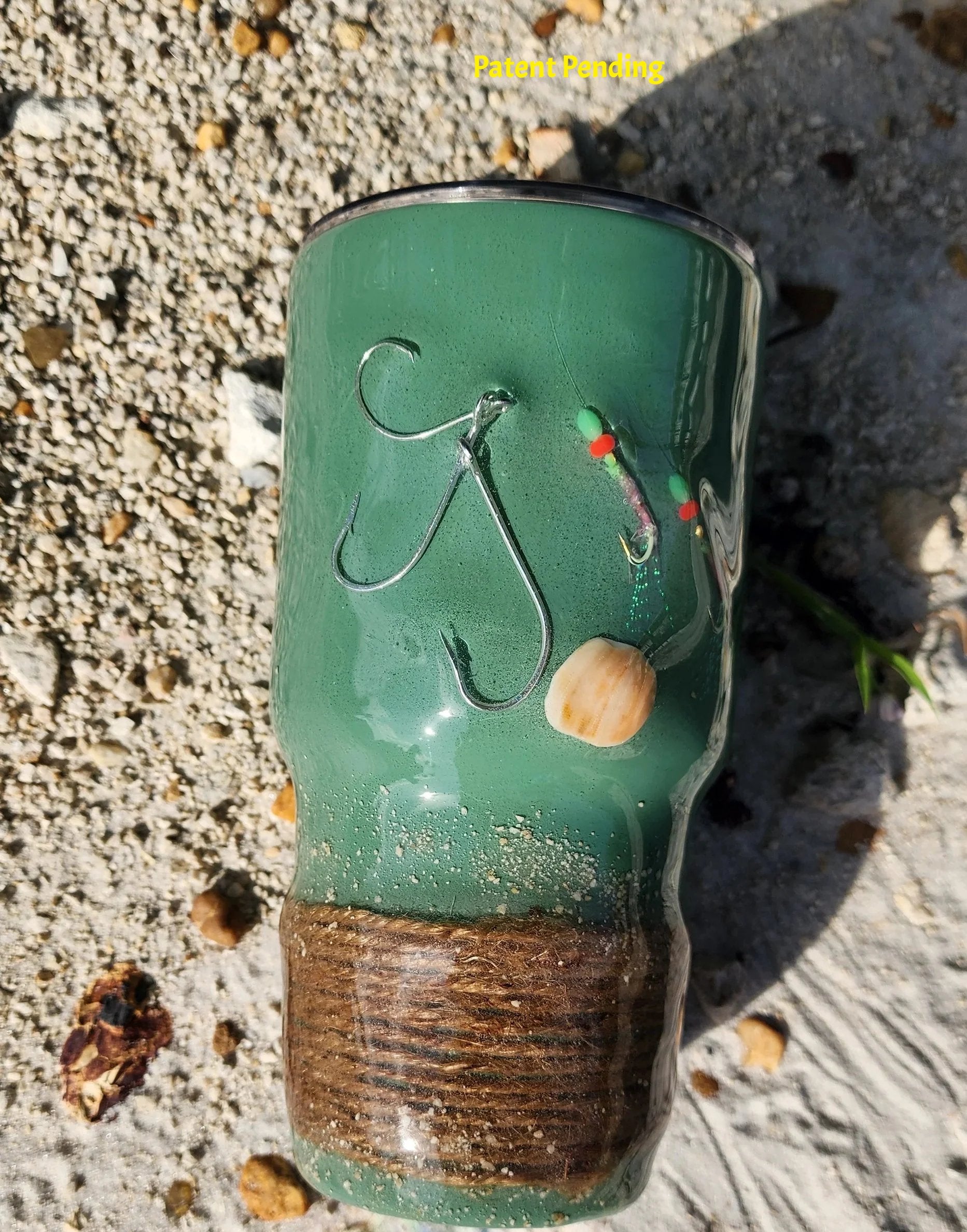Marsh Tide 30oz Hook & Tumble fishing tumbler close up on beach showing real fish hooks, glow in the dark shrimp hooks and seashell detail with natural rope wrapped base and sand