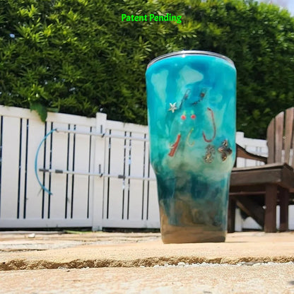 Handmade 30oz teal Caribbean coastal fishing tumbler front view - real fish hooks, glow-in-the-dark shrimp lures, silver crab and starfish charms and sea snail shells - Hook & Tumble™ by SoFlo Boho Boutique, photographed on sandy beach setting.