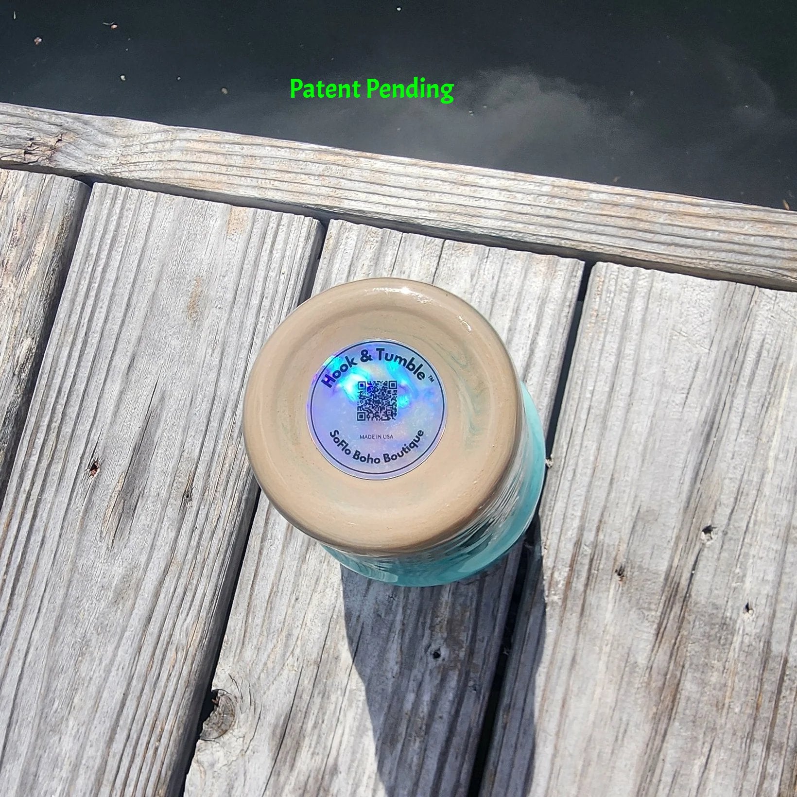 Bottom view of handmade Hook & Tumble 30oz coastal fishing tumbler showing holographic brand label with QR code, Hook & Tumble™ and SoFlo Boho Boutique branding, Made in USA - Patent Pending, displayed on South Florida marina dock.