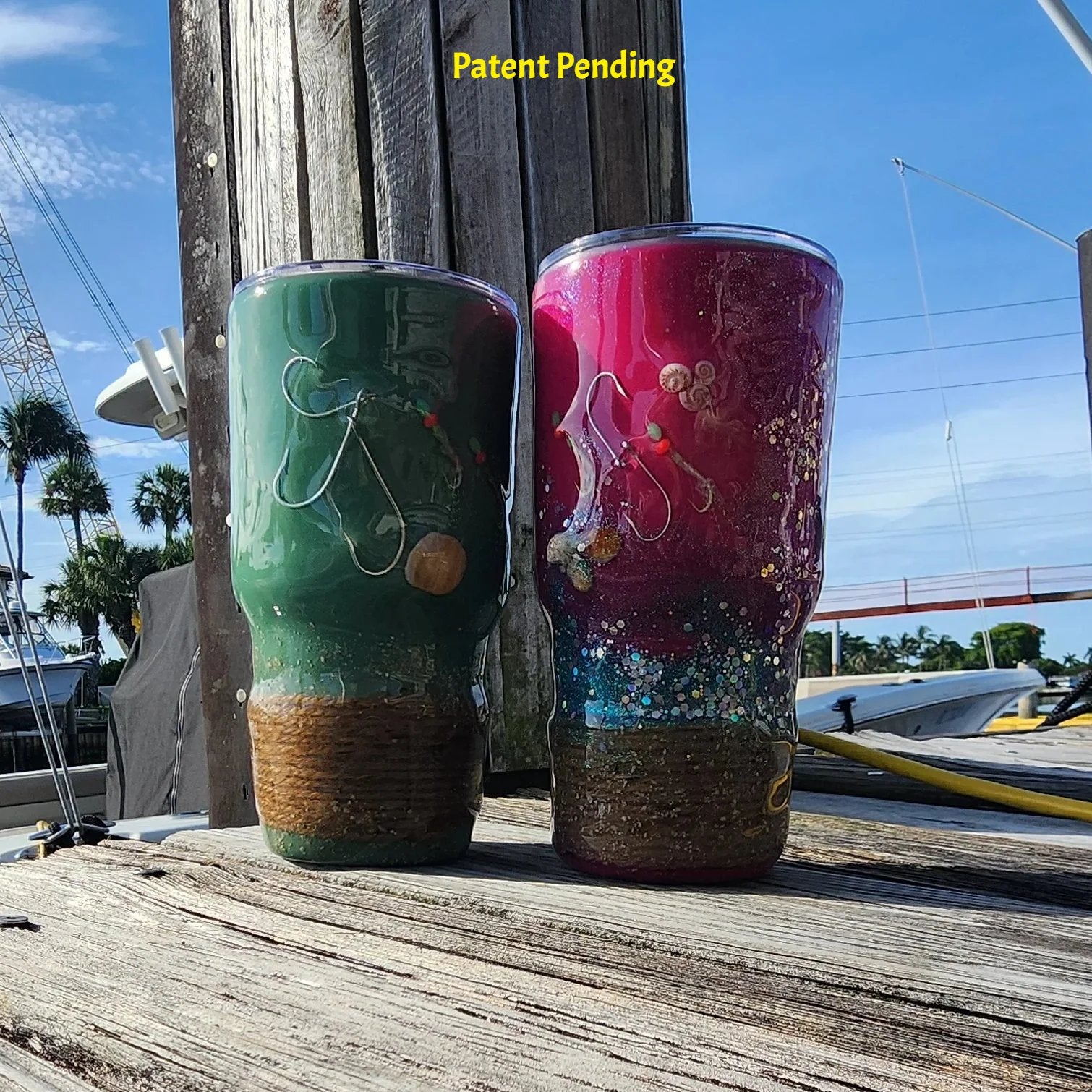 Marsh Tide and Magenta Tide Hook & Tumble 30oz fishing tumblers side by side on marina dock showing real fish hooks and seashells in crystal clear resin with natural rope wrapped bases