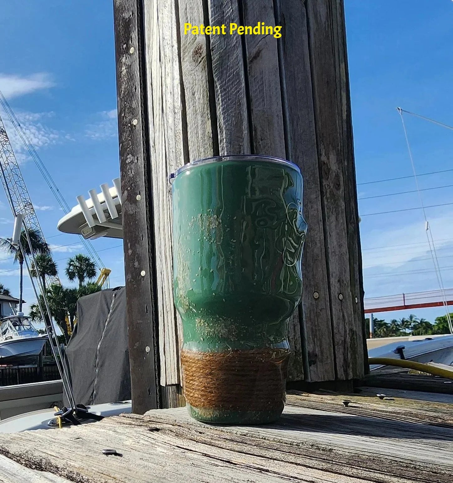 Marsh Tide 30oz Hook & Tumble Patent Pending fishing tumbler on marina dock right side view, glow in the dark shrimp hooks and seashell with natural rope wrapped base against blue sky