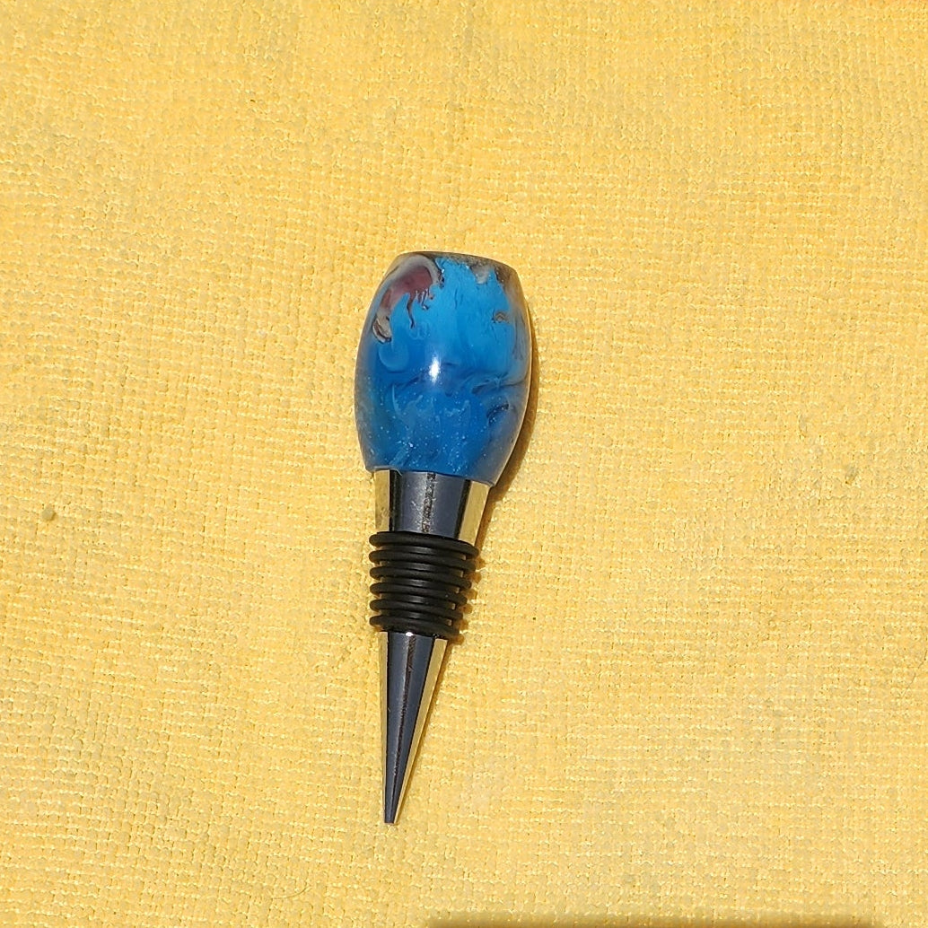 Artisan oval-shaped beach theme resin wine stopper displaying the textured sand and ocean wave layers against a yellow microfiber cloth background