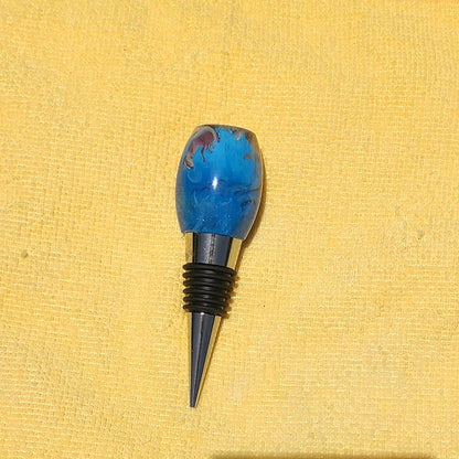 Artisan oval-shaped beach theme resin wine stopper displaying the textured sand and ocean wave layers against a yellow microfiber cloth background