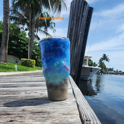 Crystal Shore Deep 30oz fishing tumbler front view on South Florida marina dock with palm trees, boat and waterway. Real saltwater fish hooks, glow-in-the-dark speckled shrimp hook and baitfish rig, sandy shore to crystal turquoise to deep cobalt blue ocean design. Hook & Tumble™ by SoFlo Boho Boutique, Patent Pending, handcrafted in South Florida.
