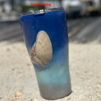 Blue ombre Saltwater Sips™ 20oz seashell tumbler front view in sand, waterfront dock background, real Florida seashell, Patent Pending