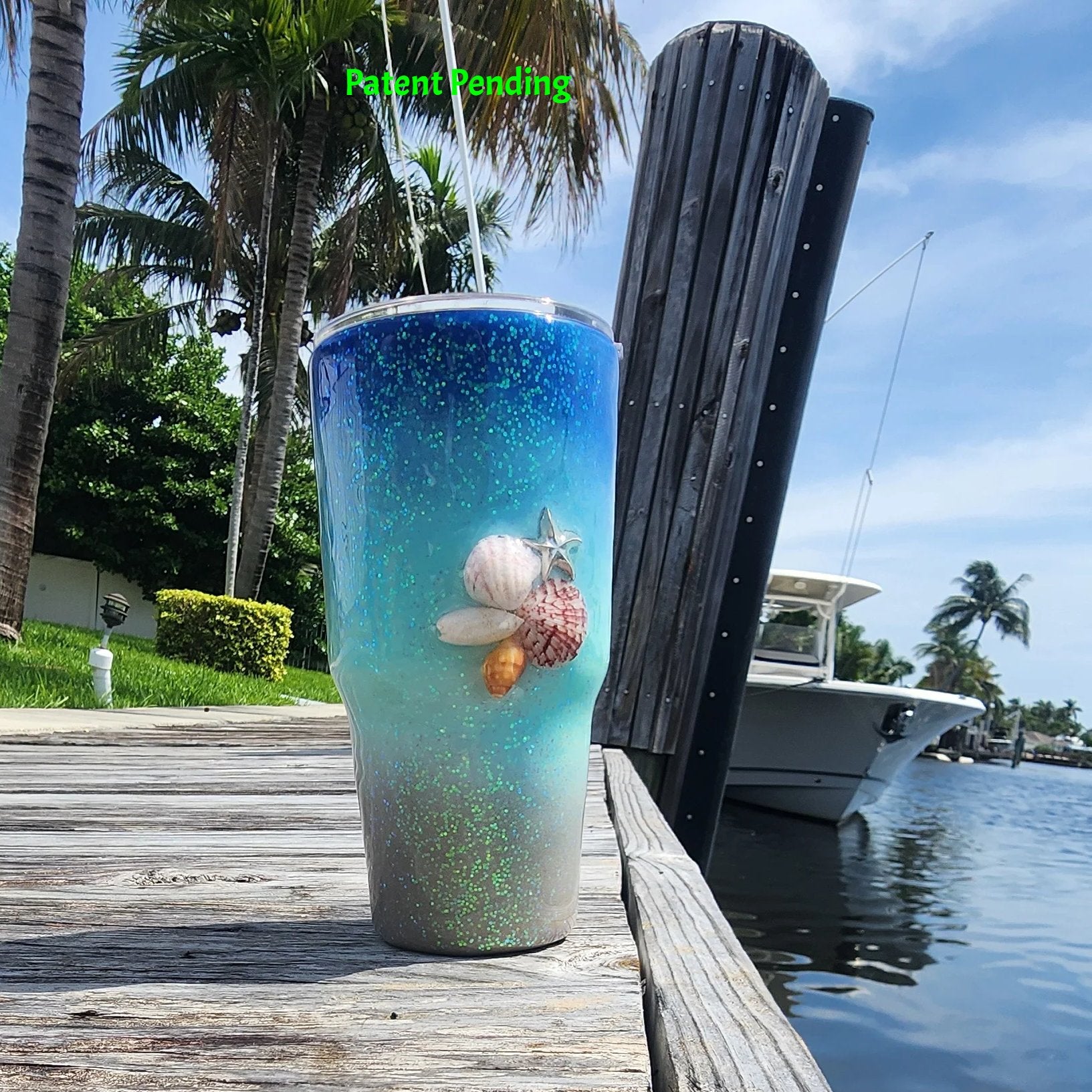 Caribbean Glow Shell Glitter 30oz tumbler front view on South Florida marina dock with real fighting conch, red, spiral and olive seashells, silver starfish charm and holographic iridescent glitter. Saltwater Sips™ by SoFlo Boho Boutique, Patent Pending, handcrafted in South Florida.