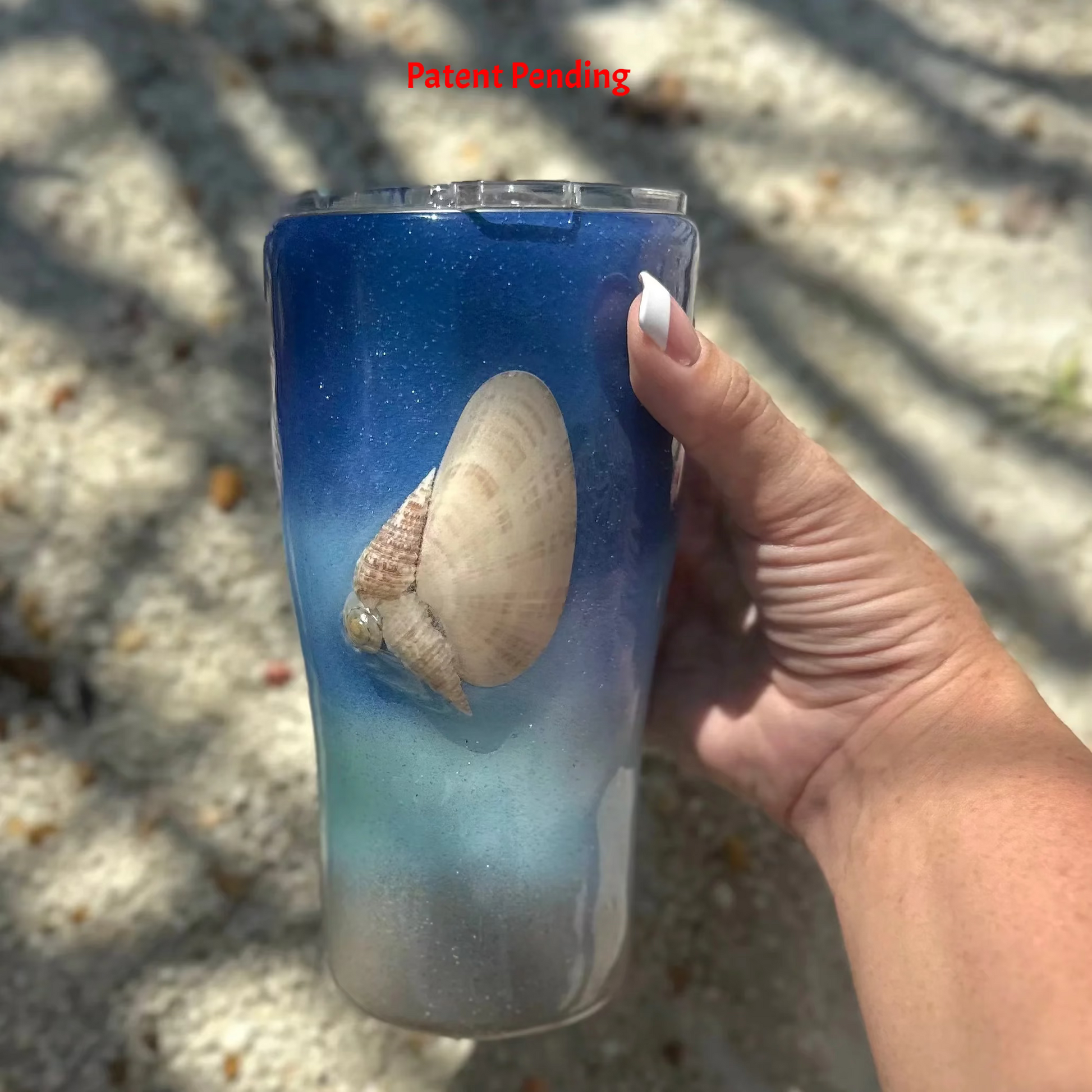Blue ombre Saltwater Sips™ 20oz seashell tumbler held in hand, real Florida seashell detail facing forward, Patent Pending, handcrafted in South Florida