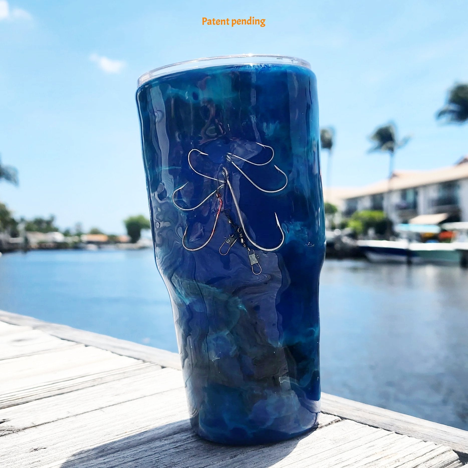 Blue Open Water close up fishing hook tumbler photographed at waterfront dock, showing deep cobalt and teal handmade 30oz coastal drinkware