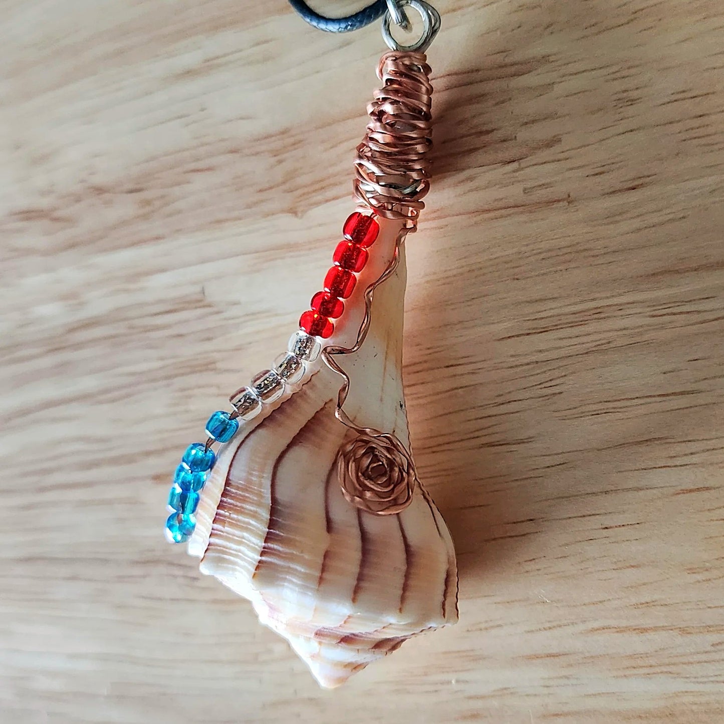 Close up of wire wrapped seashell pendant showing copper coil bail and glass bead detail on black cord